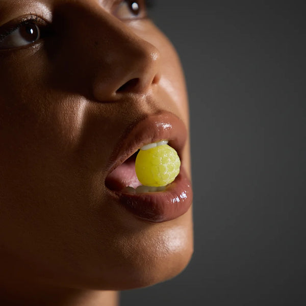 Close-up of a person holding a yellow gummy near their mouth against a dark background
